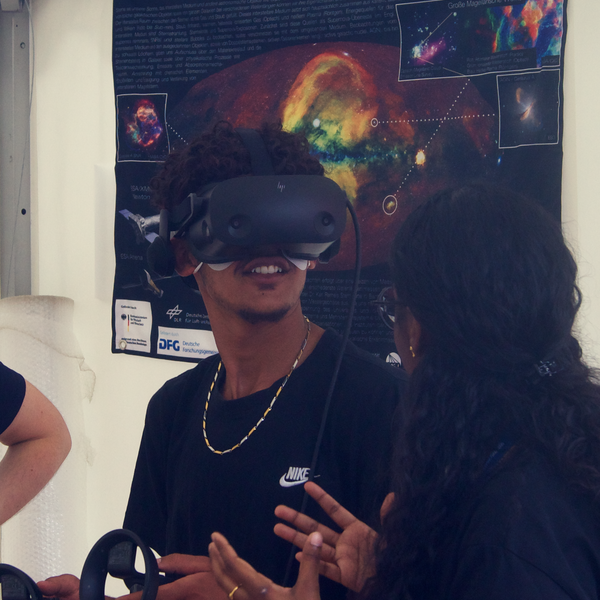 Ein Mann trägt eine VR Brille in einem Zelt, hinter ihm hängt ein Poster von einem Planetarium