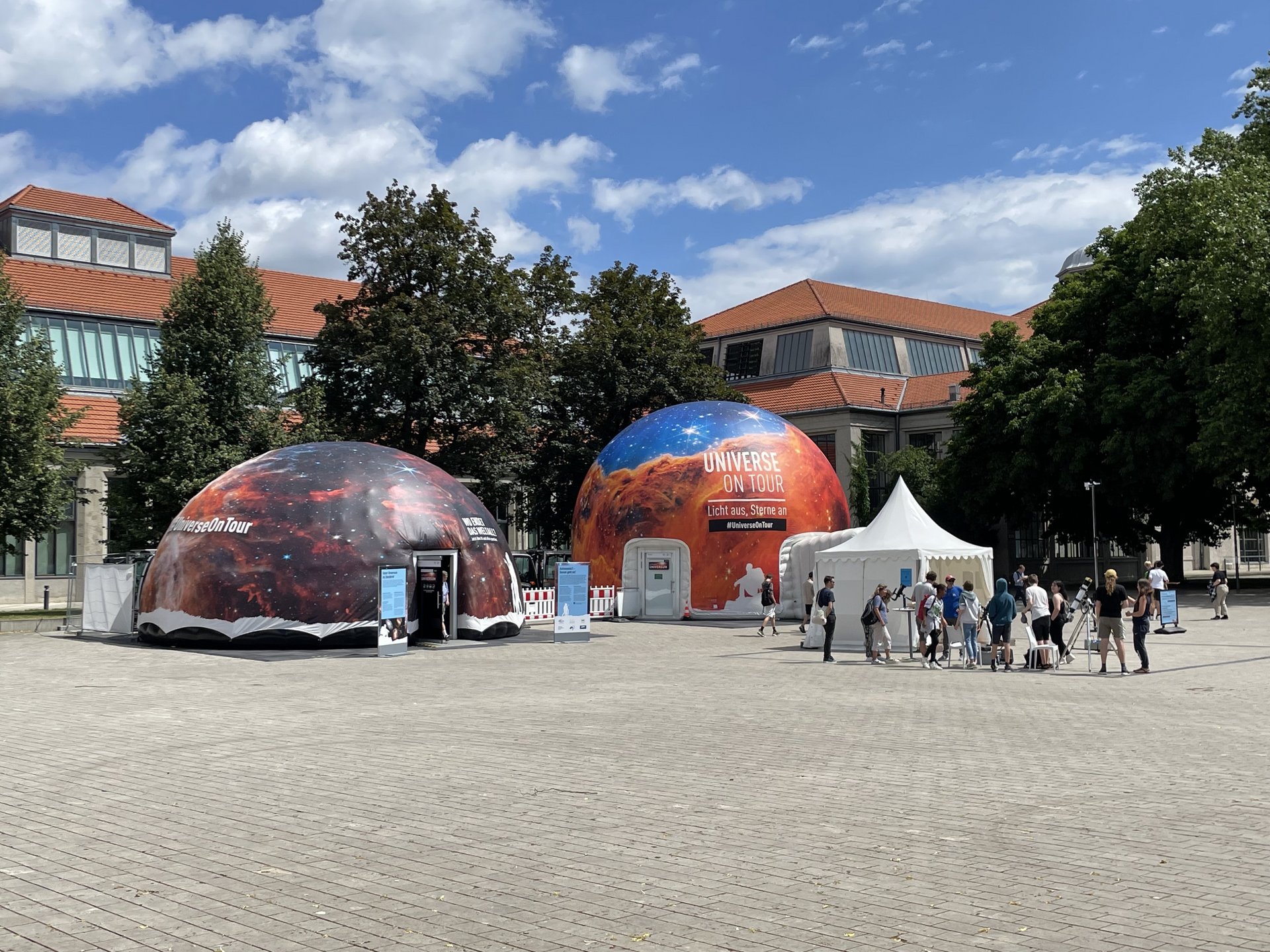 Foto der zwei Kuppelzelte, vor ihnen stehen Menschen um ein Teleskop herum