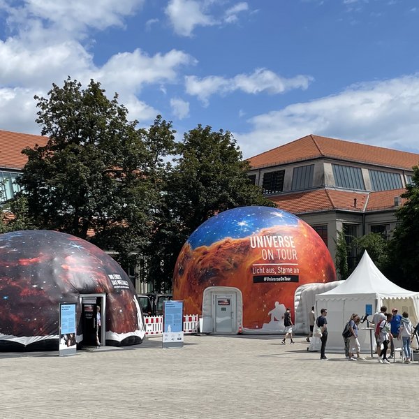 Foto der zwei Kuppelzelte, vor ihnen stehen Menschen um ein Teleskop herum