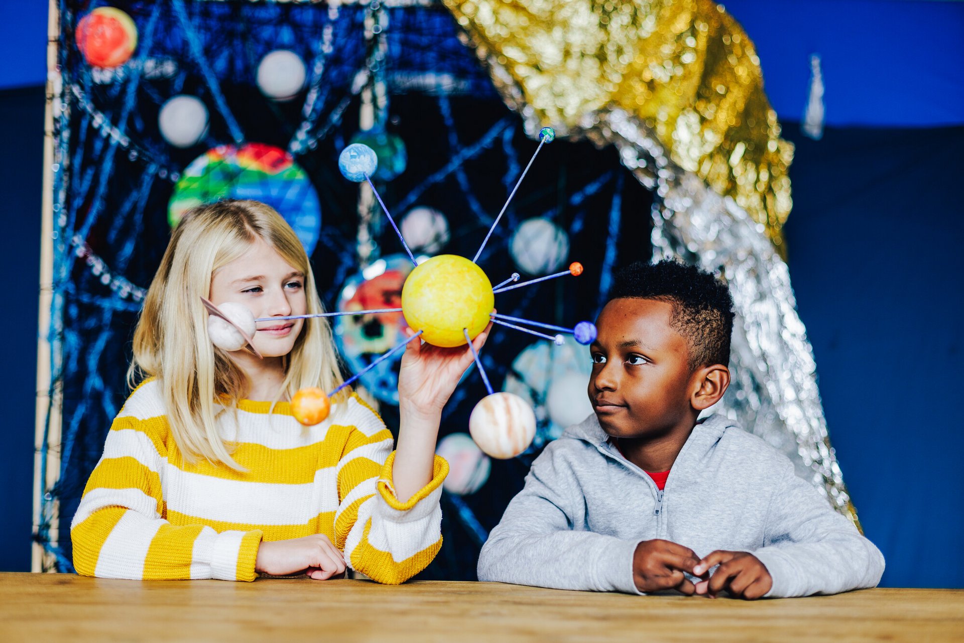 Zwei Kinder halten ein illustriertes Sonnensystem in der Hand.