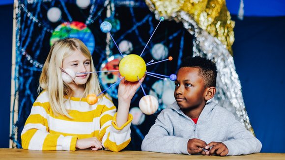 Zwei Kinder halten ein illustriertes Sonnensystem in der Hand.