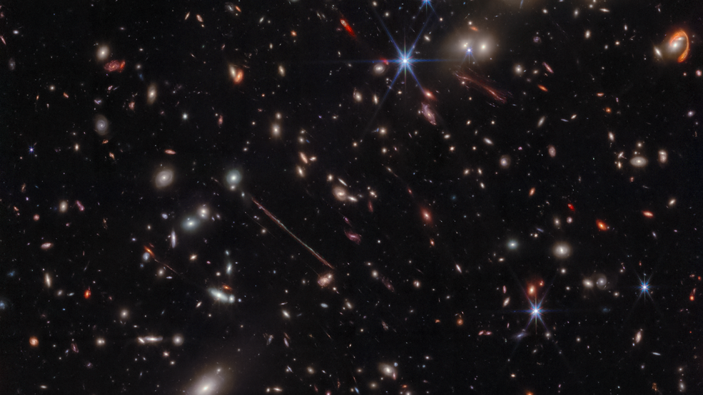 Ein dunkler Hintergrund mit vielen verschwommenen Flecken darauf. In der Mitte ist eine blasse Linie, rechts oben ein knalloranger, hakenförmiger Bogen