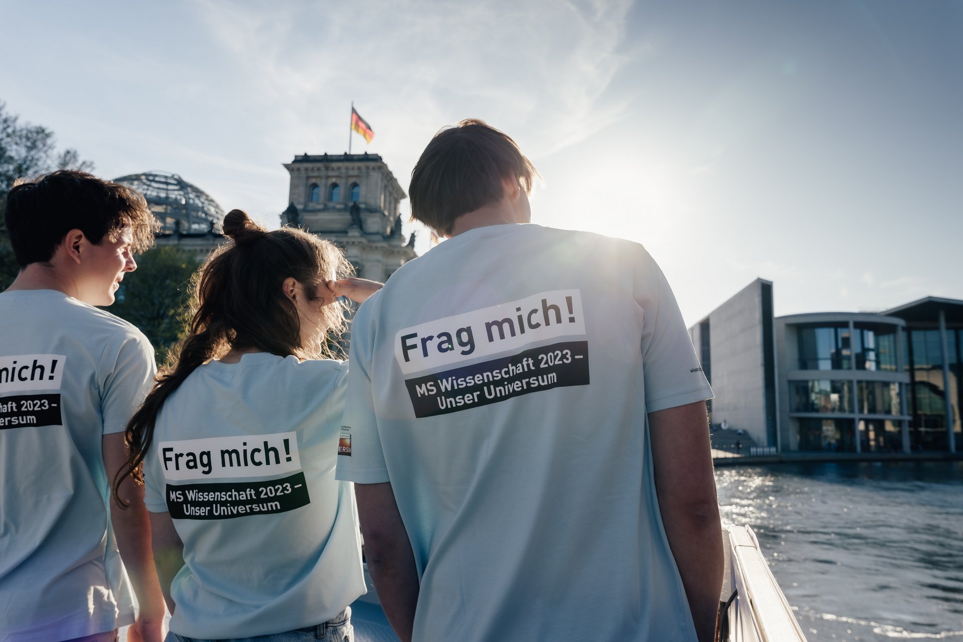 Drei Personen von hinten, Aufdruck auf den "T-Shirts: Frag mich! MS Wissenschaft". 