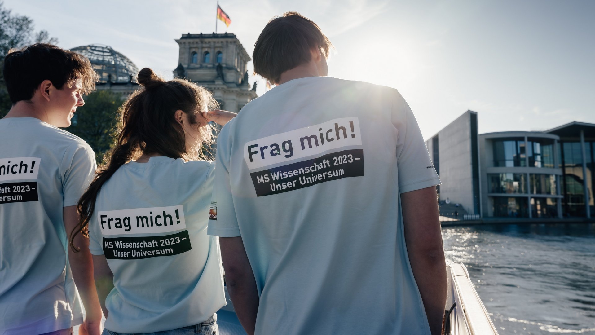 Drei Personen von hinten, Aufdruck auf den "T-Shirts: Frag mich! MS Wissenschaft". 