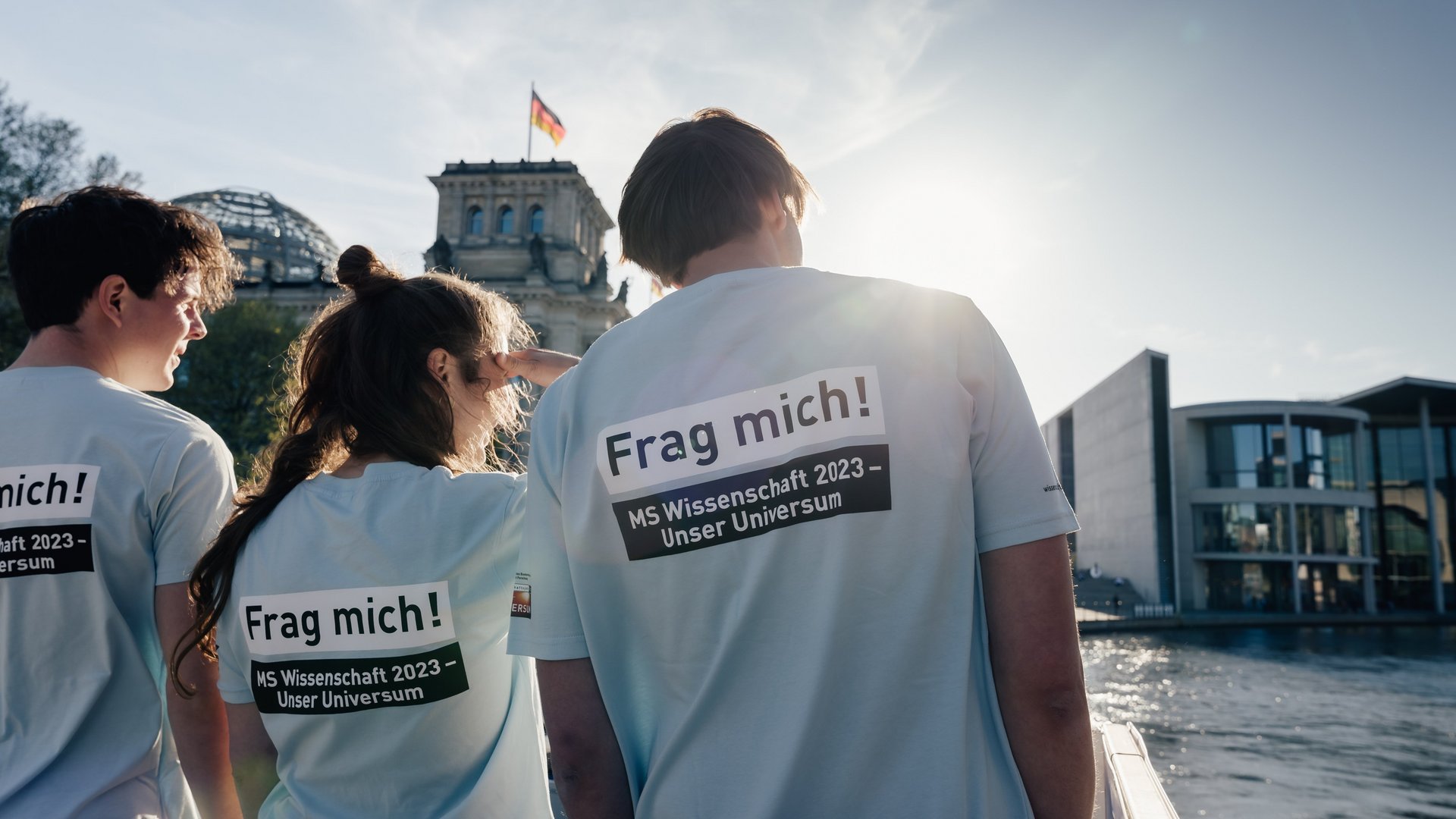 Drei Personen von hinten, Aufdruck auf den "T-Shirts: Frag mich! MS Wissenschaft". 