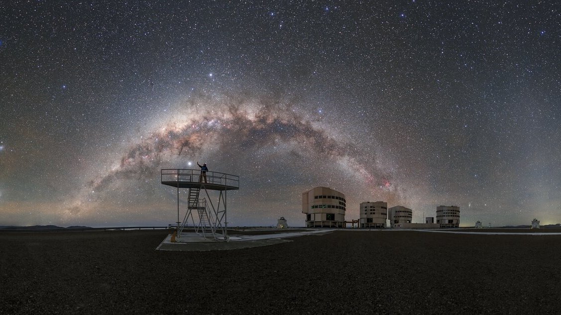 Milchstraße über den vier Teleskopen des Very Large Telescope, davor steht eine Person auf einem Gerüst.