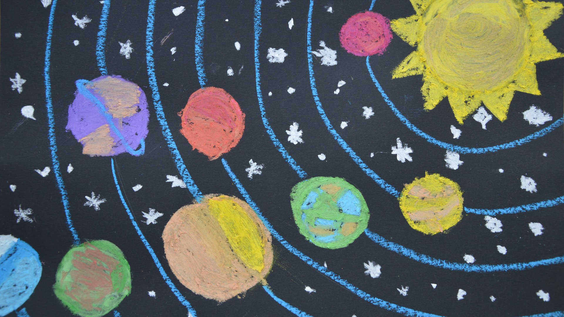Das Sonnensystem ist mit bunter Kreide an eine dunkle Wand gemalt.