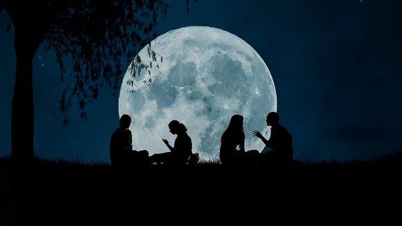 Silhouetten von vier Menschen, die vor dem Vollmond sitzen