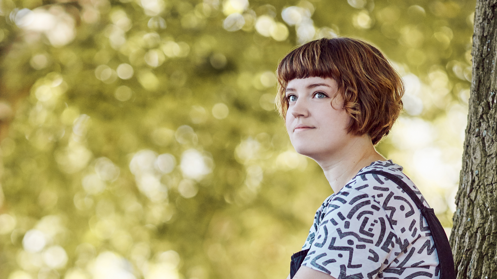 Foto von Maren Hasenjäger: Profilansicht, sie lehnt an einem Baum und schaut in die Ferne.
