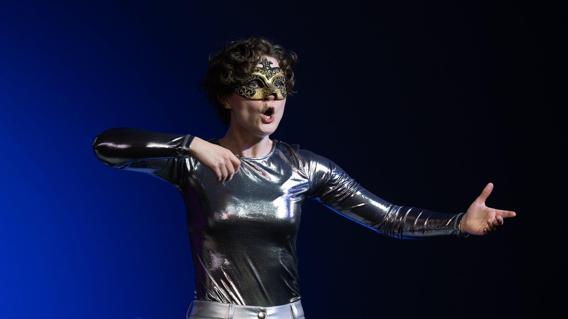 Eine maskierte Schauspielerin gestikuliert.