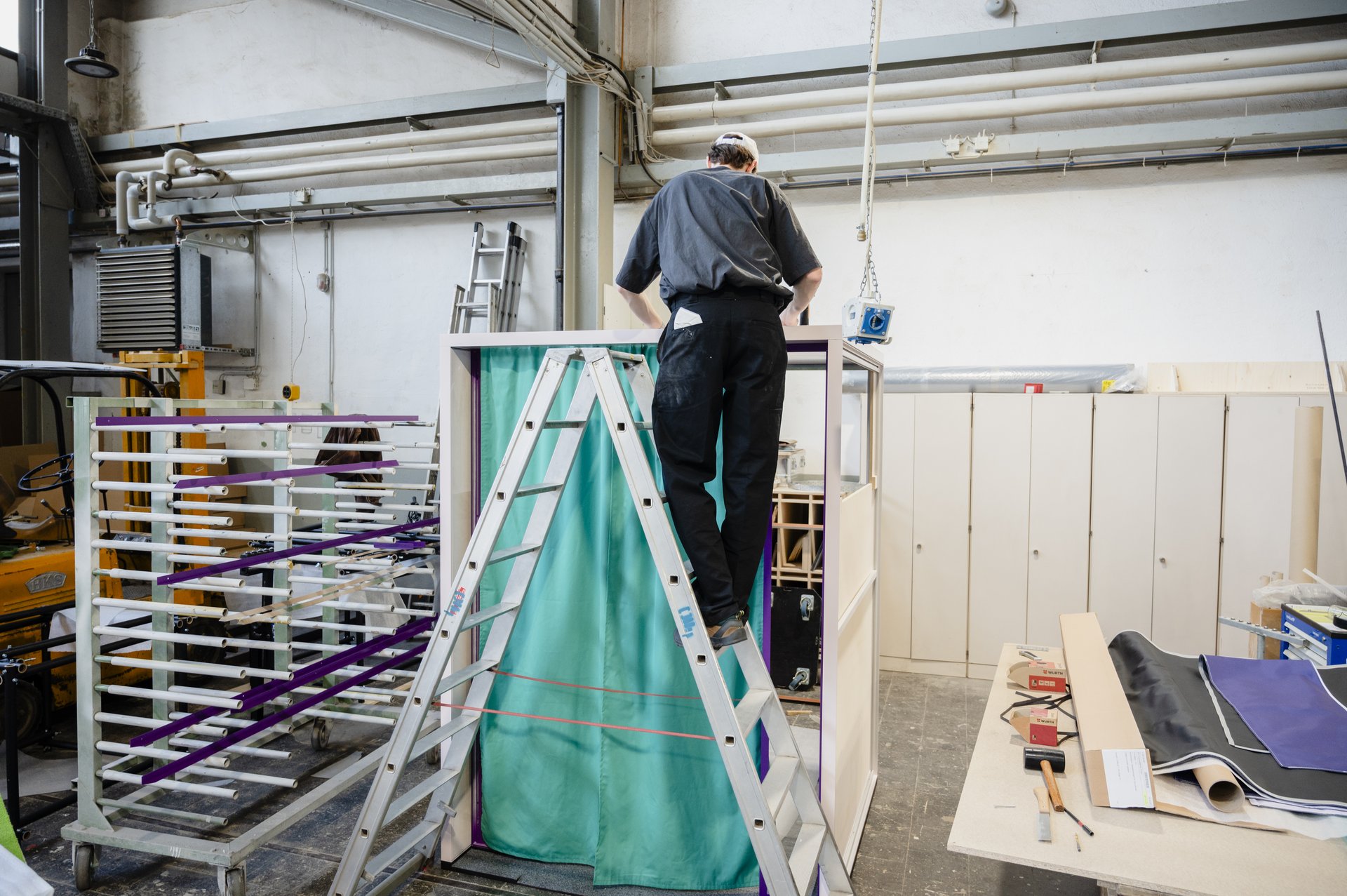 Eine Person steht auf einer Leiter vor der Erzählbox und befestigt den Vorhang.