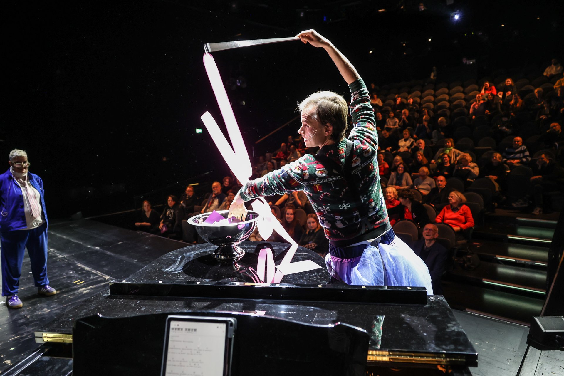 Ein Darstelle tanzt auf der Bühne mit einem Gymnastikband und zieht dabei einen Zettel aus dem Publikum.