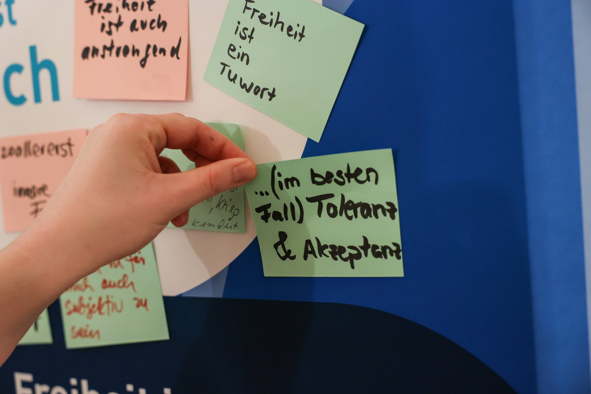 Eine Person klebt einen Zettel mit der Aufschrift „Im besten Fall Toleranz & Akzeptanz“ auf eine Tafel.