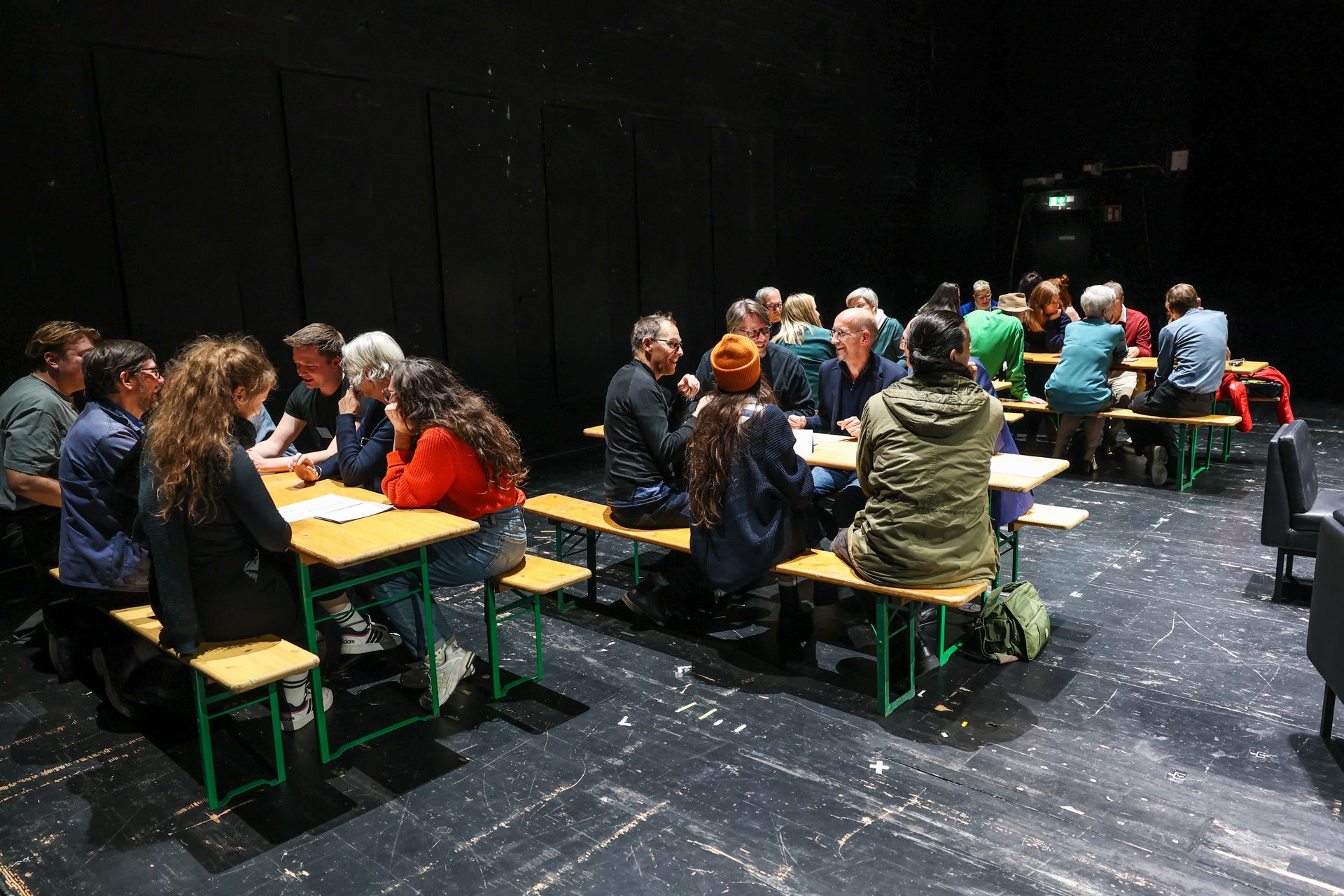 Mehrere Tischgruppen auf der Theaterbühne im Gespräch.