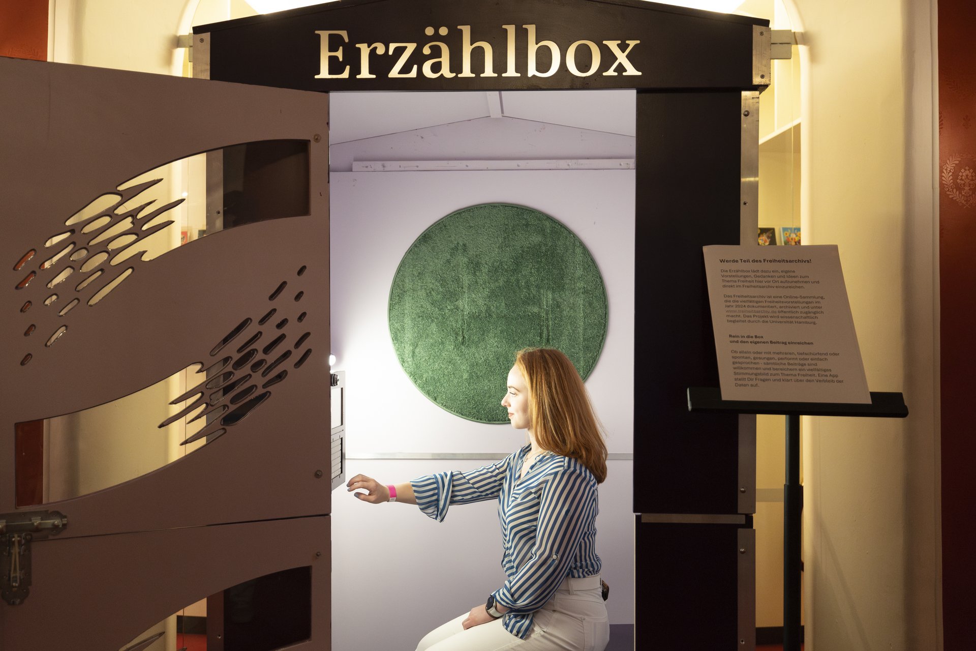 Eine junge Frau sitzt in der Erzählbox und bedient den Touchscreen.