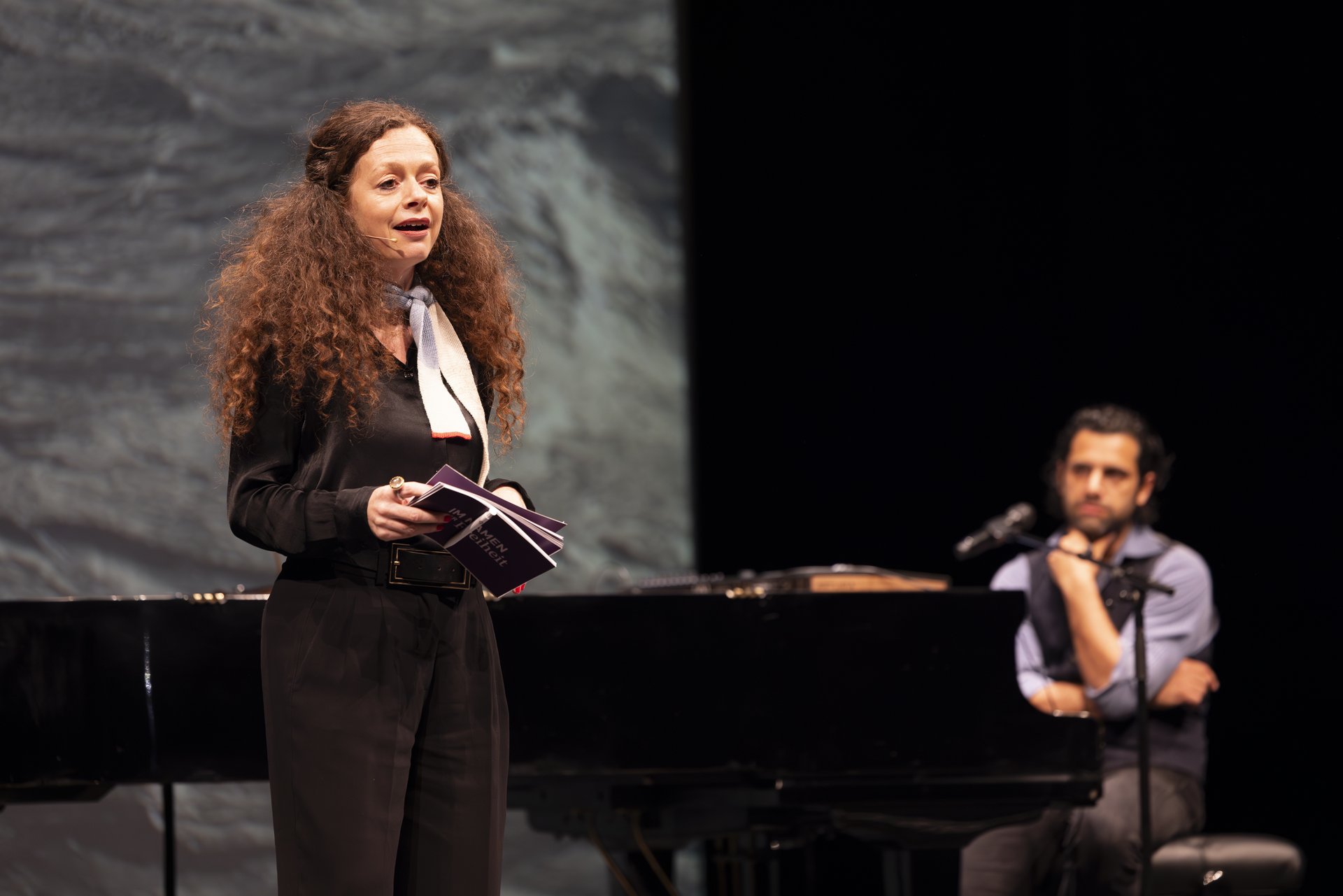Moderatorin Shelly Kupferberg auf der Bühne. Im Hintergrund sitzt Gabriel Cazes am Klavier. 