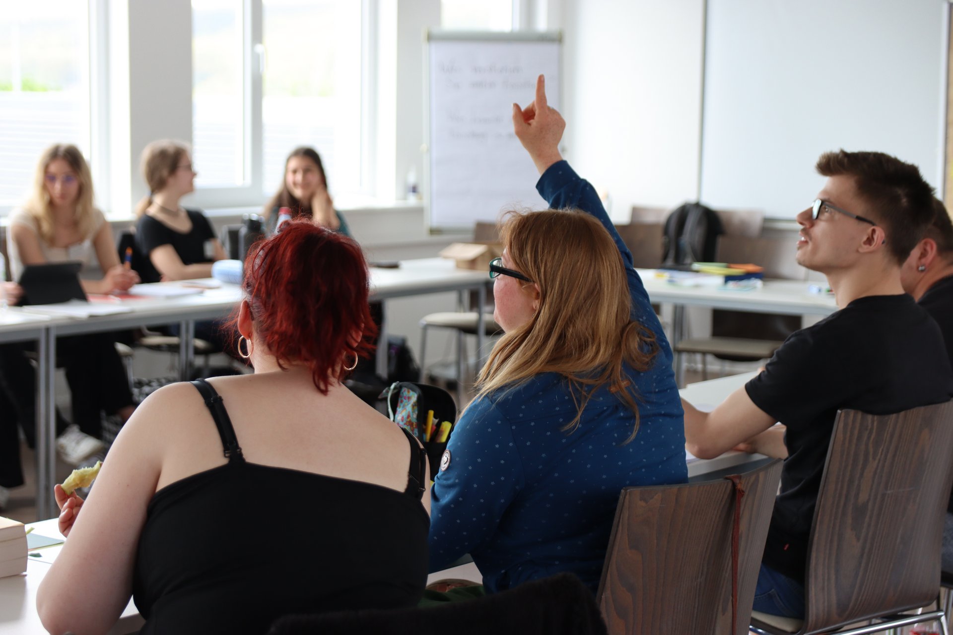 Eine Frau meldet sich in einem Seminarraum mit weiteren Menschen.