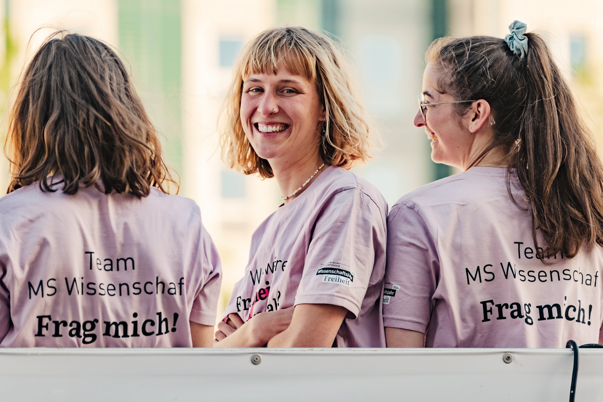 Drei Studierende in fliederfarbenen T-Shirts der Mitarbeitenden der MS Wissenschaft.