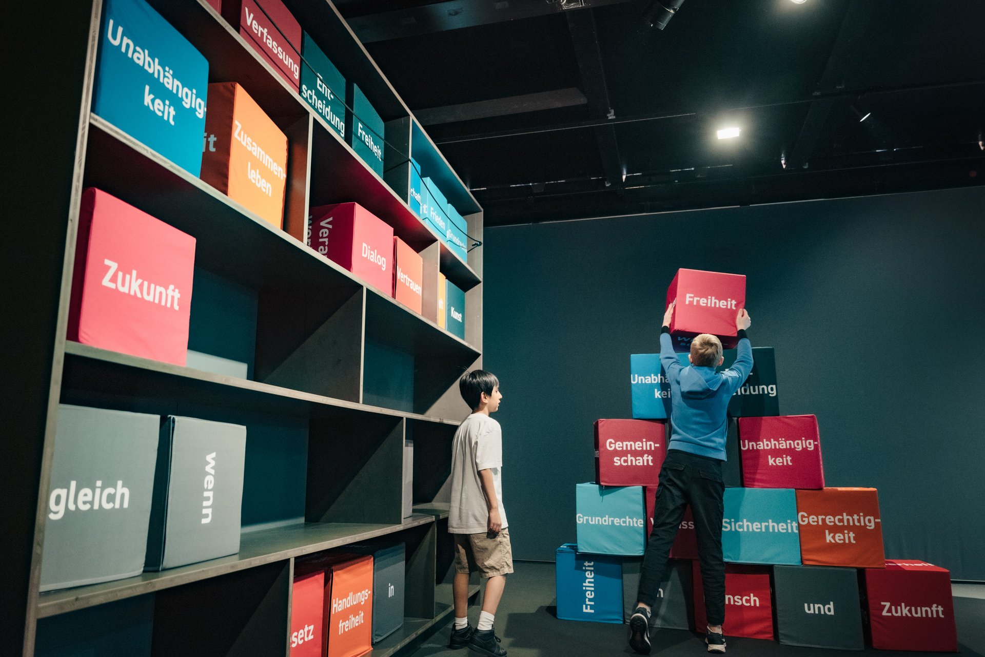 Zwei Kinder bauen eine Pyramide aus Blöcken mit verschiedenen Begriffen zum Thema Freiheit.
