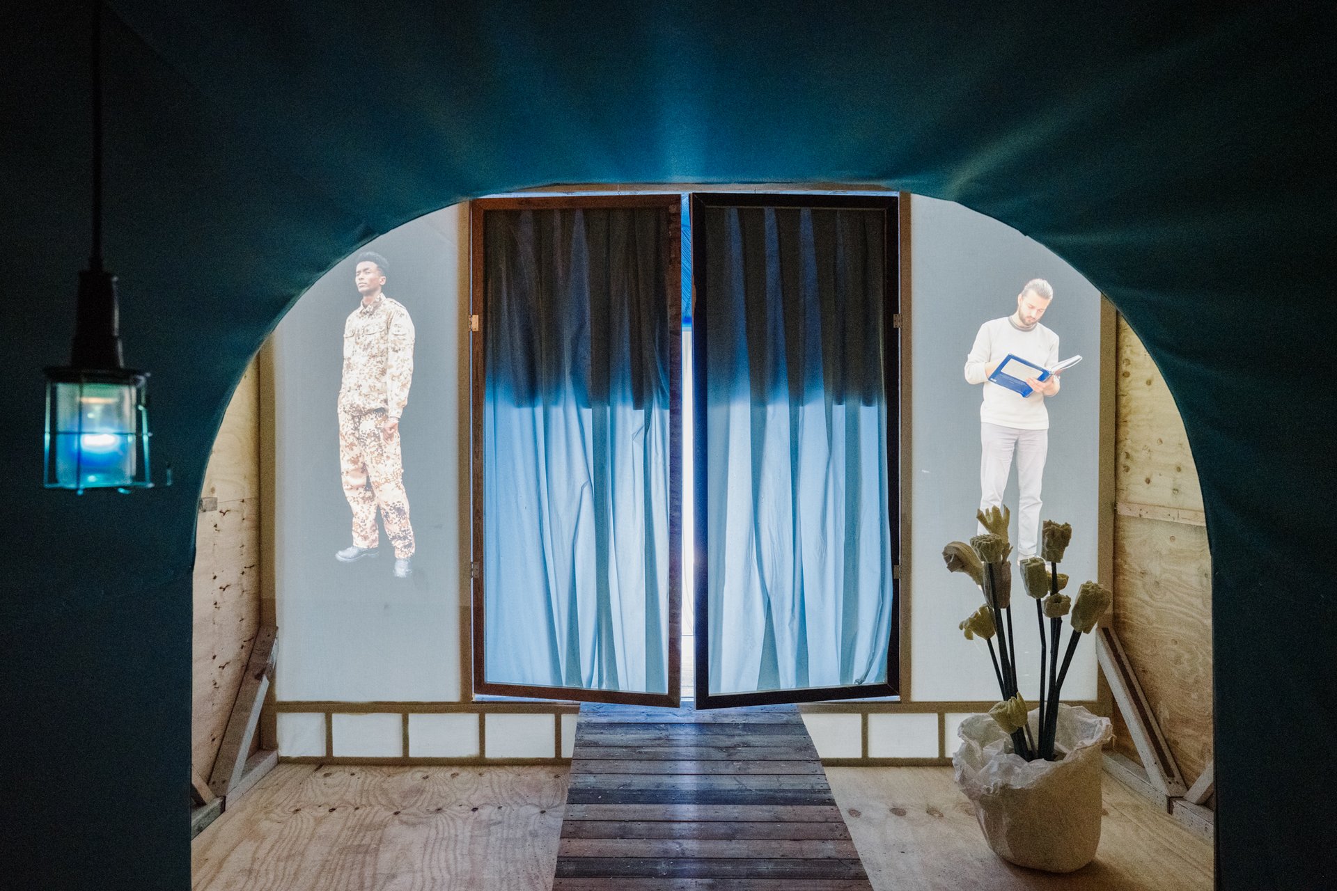 Foto einer Kunstausstellung mit Projektionen von einem Soldaten und einem lesenden Mann.