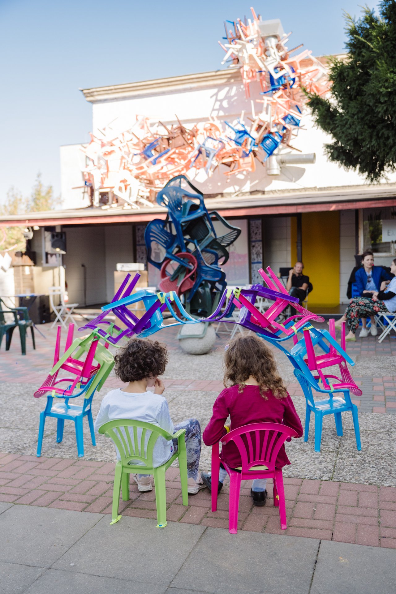 Zwei Kinder betrachten einen Turm aus Plastikstühlen.