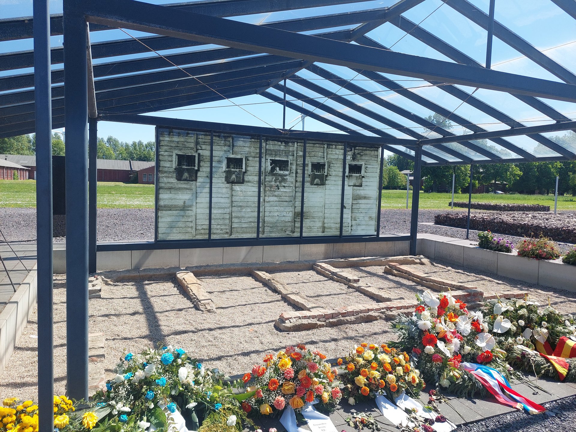 Gedenkstätte mit Blumensträußen im Vordergrund.