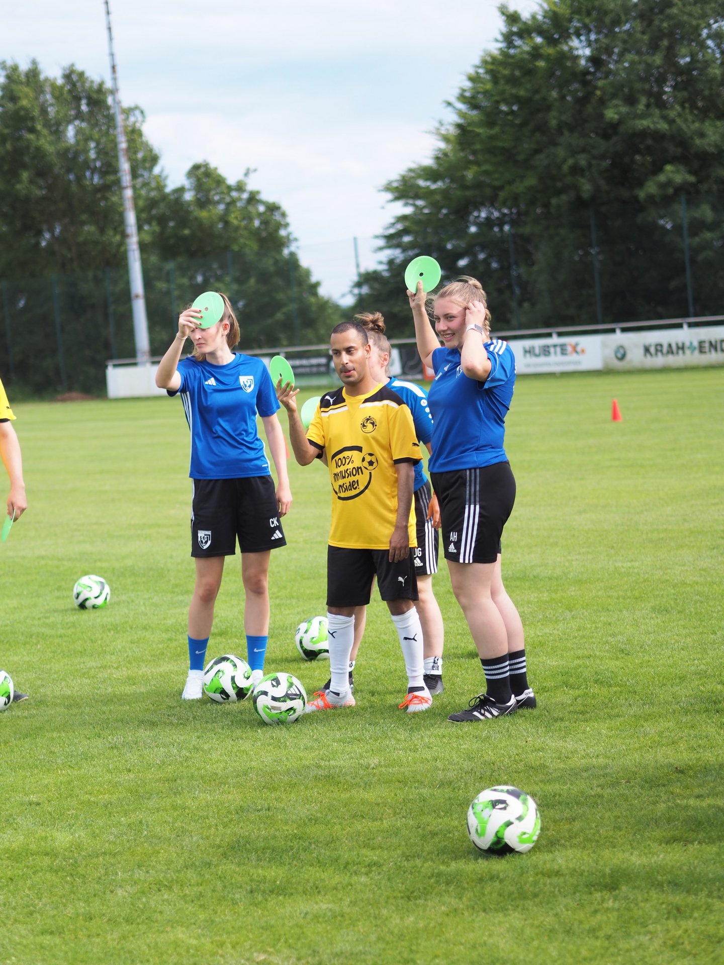 Menschen mit und ohne Behinderung halten beim Fußballtraining bunte Scheiben in der Hand.