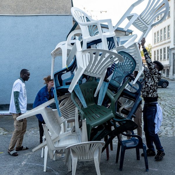 Junge Menschen stapeln Plastikstühle.