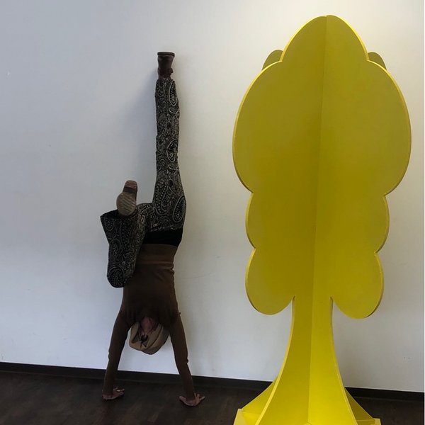 Foto einer Person, die einen Kopfstand neben einem gelben Baummodell macht.