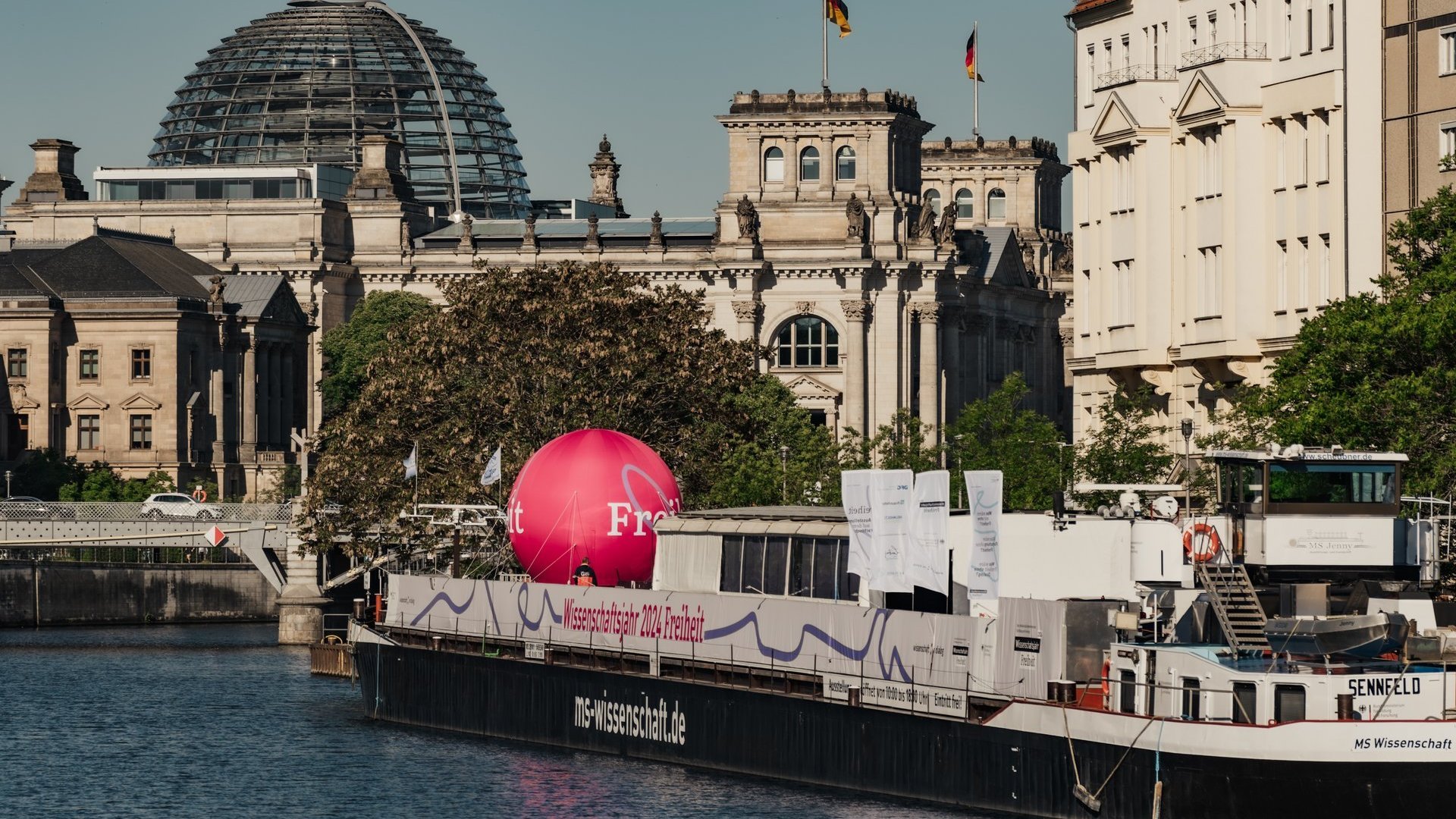 Die MS Wissenschaft im Hafen in Berlin. Im Hintergrund ist die Kuppel des Reichstags.