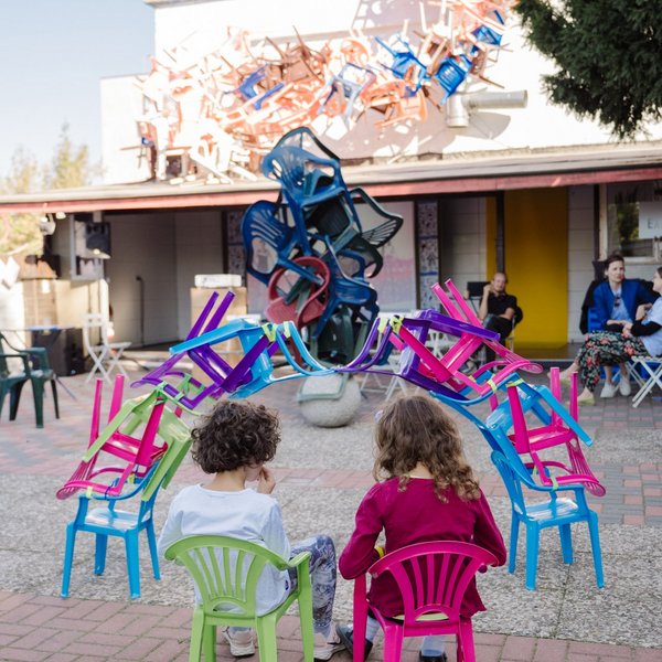 Zwei Kinder betrachten einen Turm aus Plastikstühlen.