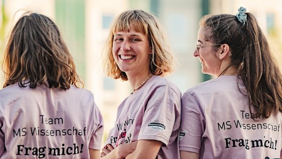 Drei Studierende in fliederfarbenen T-Shirts der Mitarbeitenden der MS Wissenschaft.
