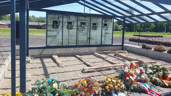 Gedenkstätte mit Blumensträußen im Vordergrund.