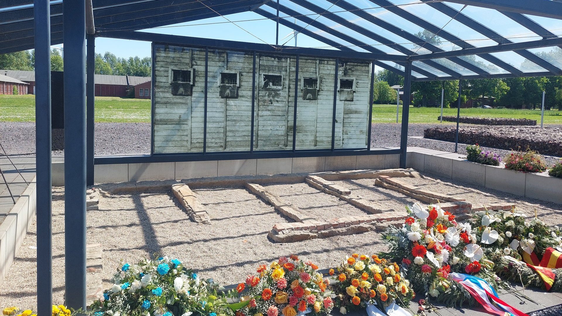 Gedenkstätte mit Blumensträußen im Vordergrund.