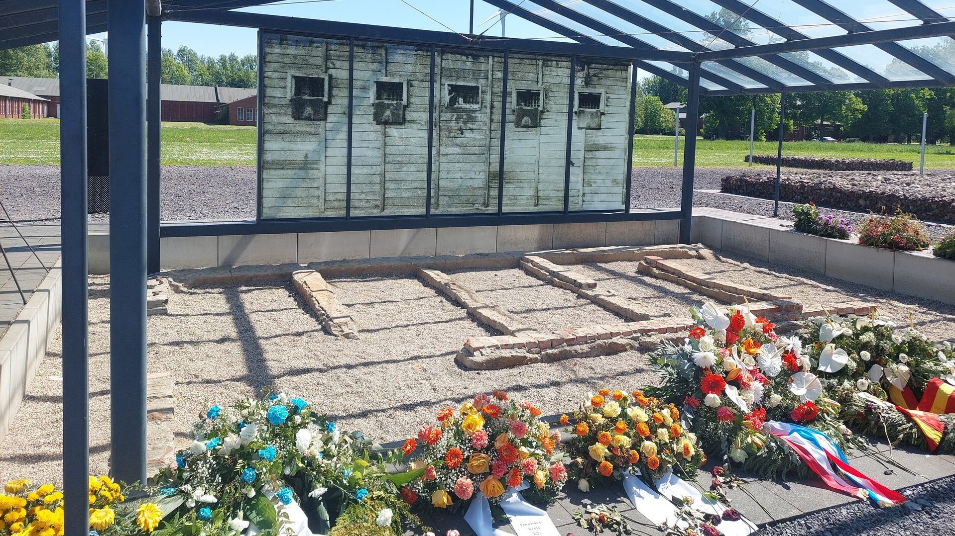 Gedenkstätte mit Blumensträußen im Vordergrund.