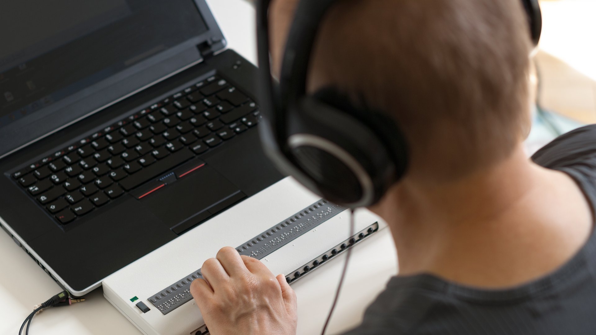 Eine sehbehinderte Person benutzt einen Braille Display und einen Screenreader.