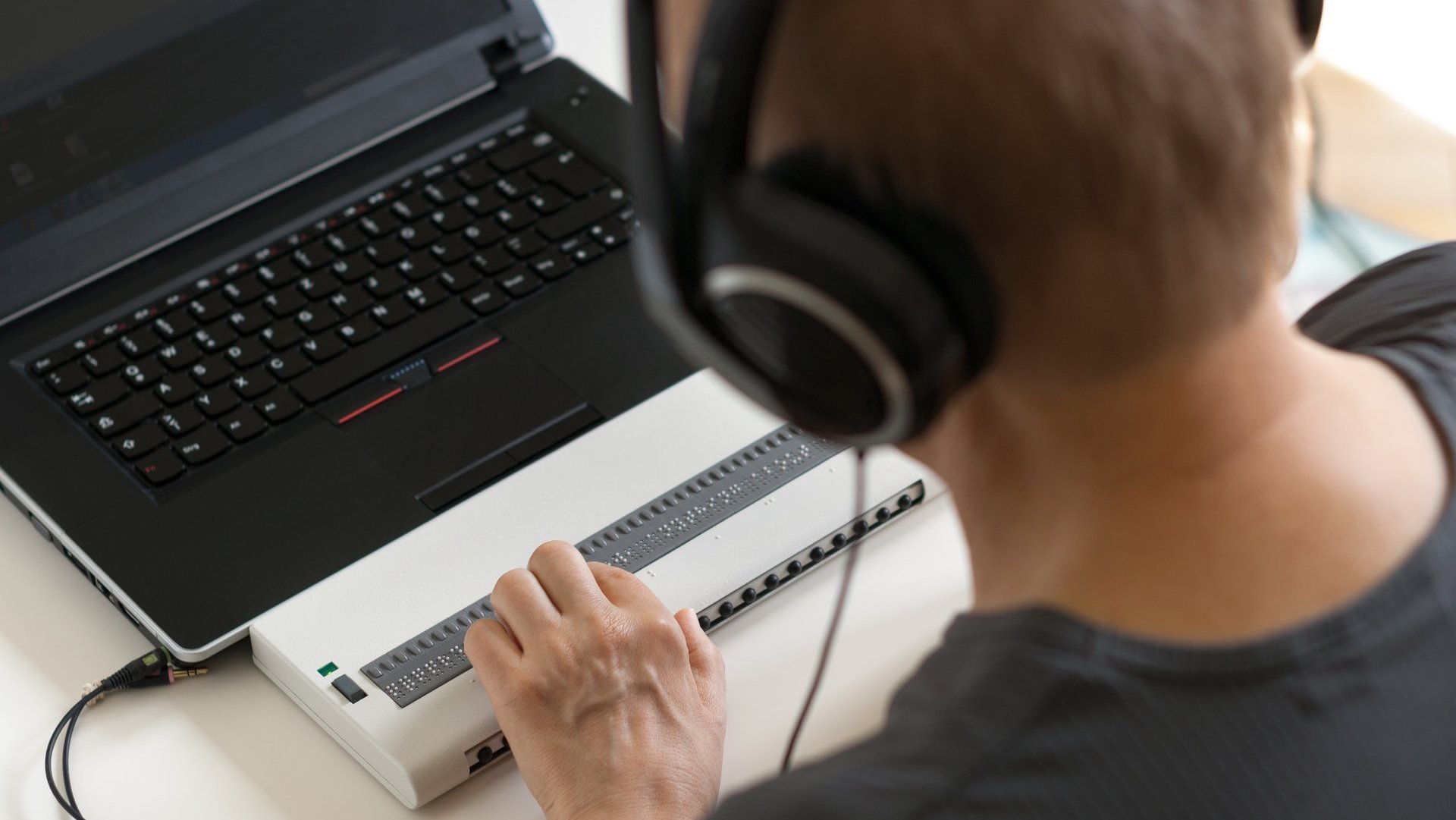 Eine sehbehinderte Person benutzt einen Braille Display und einen Screenreader.