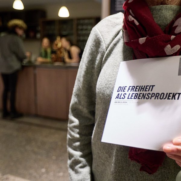 Eine Person hält einen Flyer mit der Aufschrift „Freiheit als lebensprojekt“.