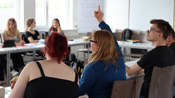 Eine Frau meldet sich in einem Seminarraum mit weiteren Menschen.
