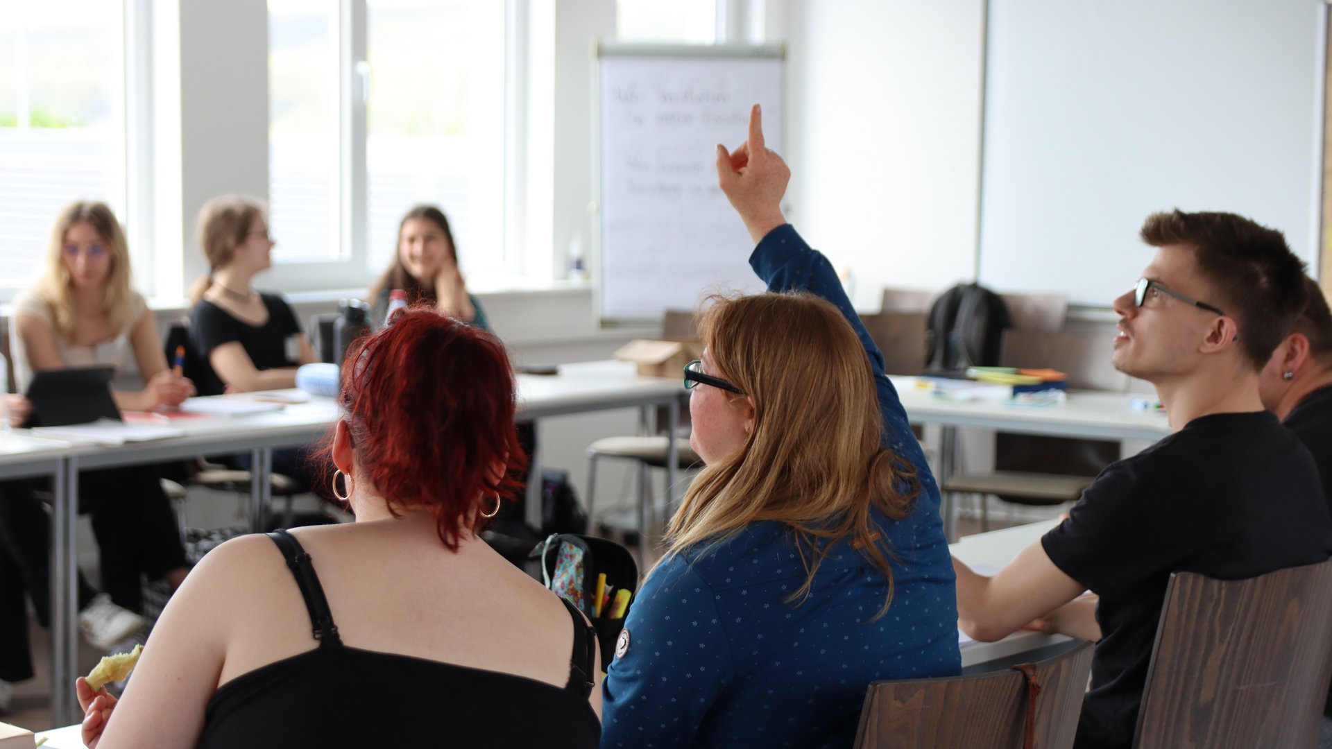 Eine Frau meldet sich in einem Seminarraum mit weiteren Menschen.