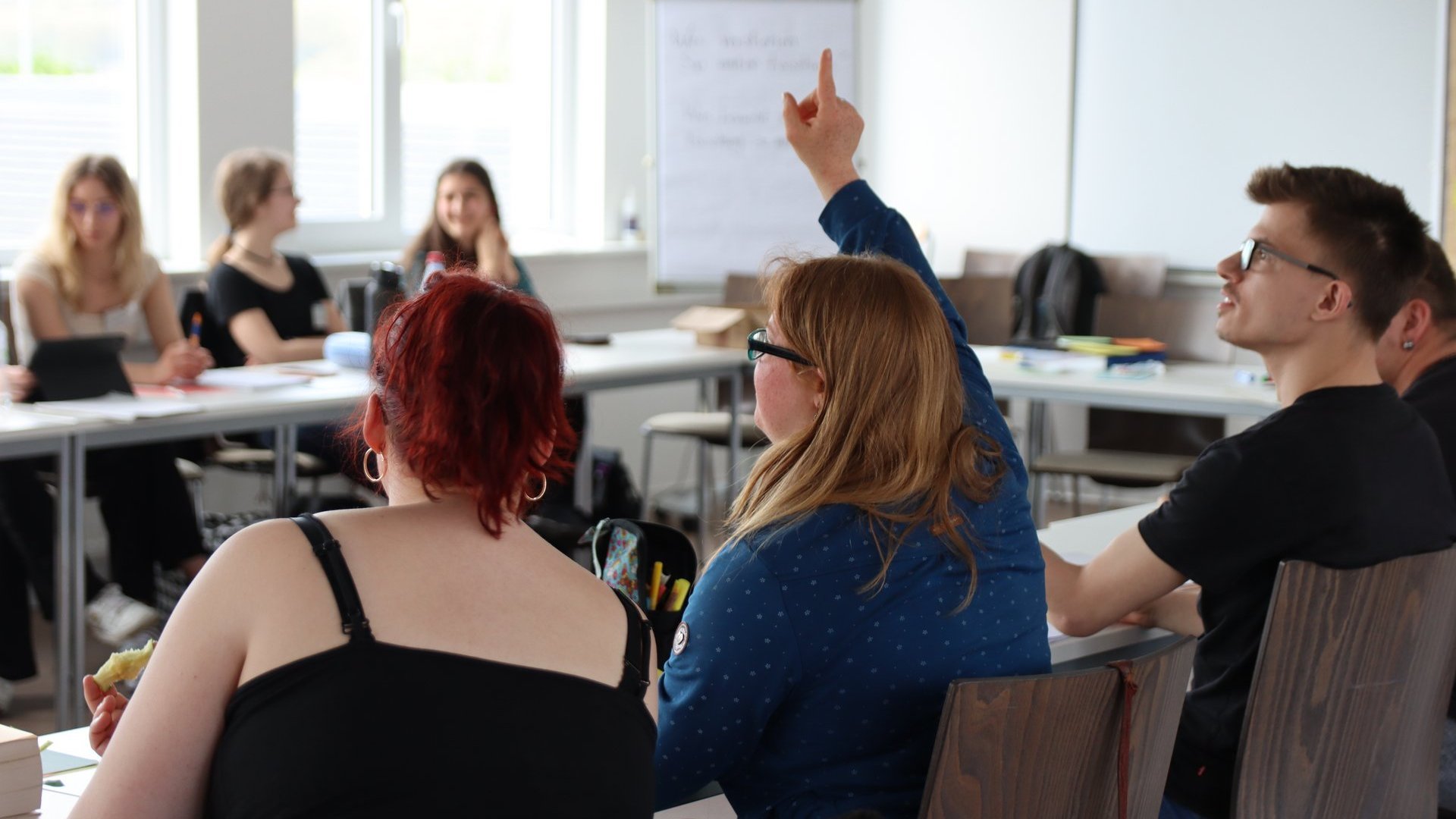 Eine Frau meldet sich in einem Seminarraum mit weiteren Menschen.