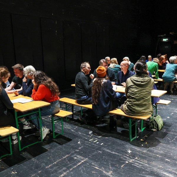 Mehrere Tischgruppen auf der Theaterbühne im Gespräch.