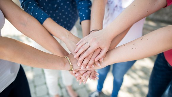 Vier Menschen stehen im Kreis und legen in der Mitte ihre Hände übereinander.