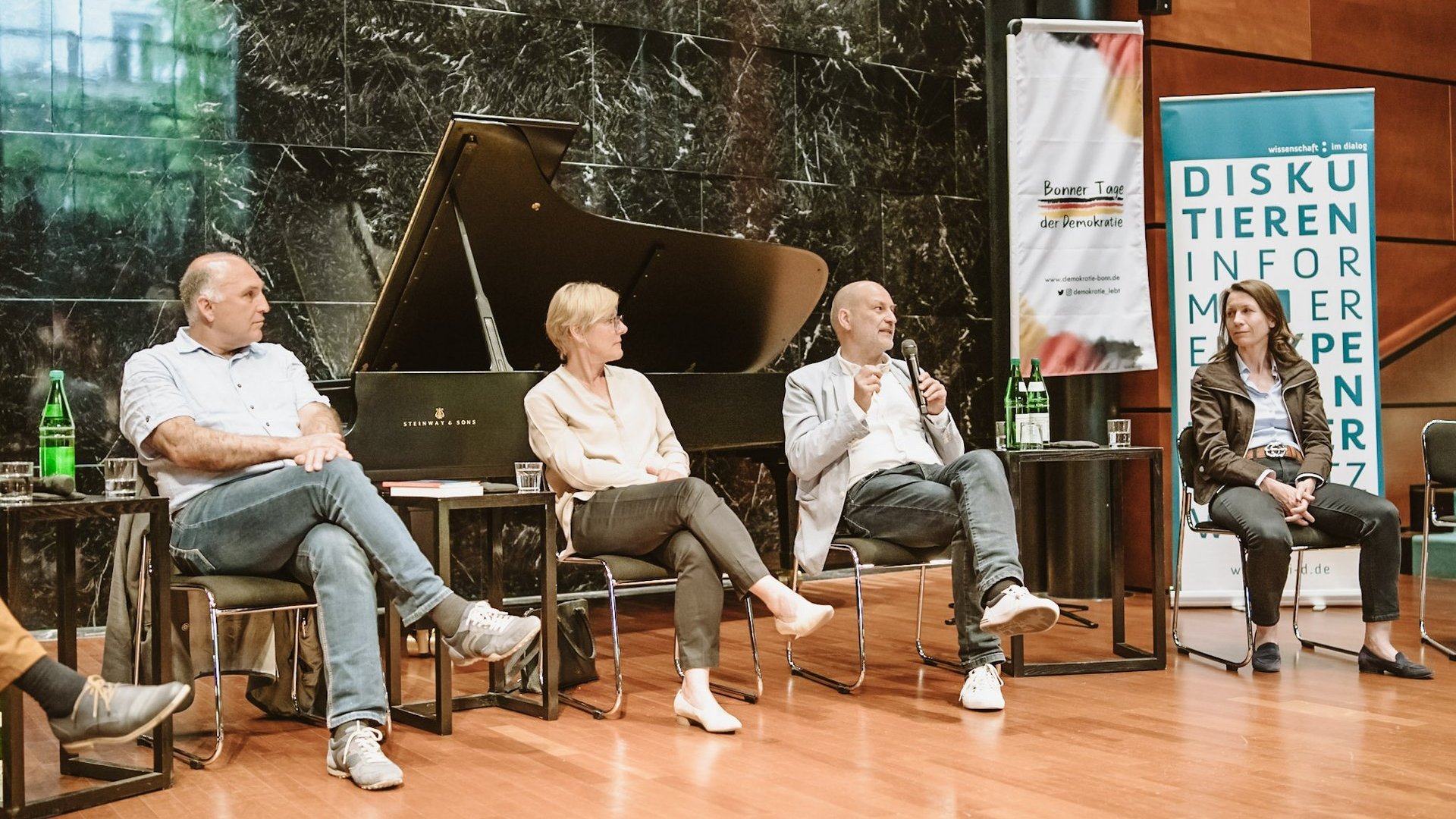 Vier Wissenschaftlerinnen und Wissenschaftler diskutieren auf einer Bühne.