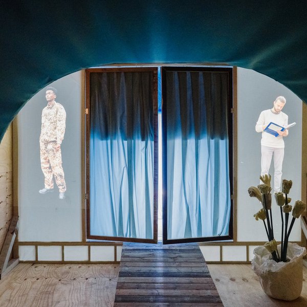 Foto einer Kunstausstellung mit Projektionen von einem Soldaten und einem lesenden Mann.