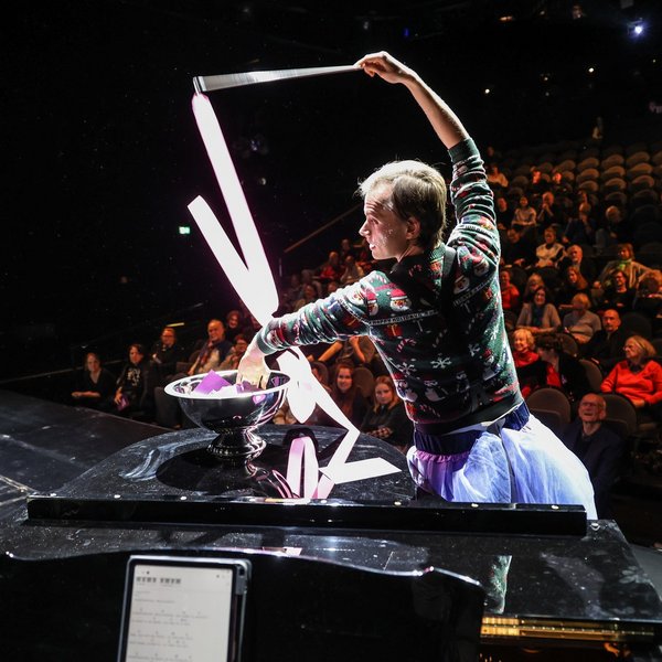 Ein Darstelle tanzt auf der Bühne mit einem Gymnastikband und zieht dabei einen Zettel aus dem Publikum.