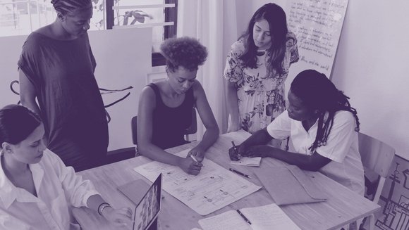 Foto einer Arbeitsgruppe um einen Schreibtisch.