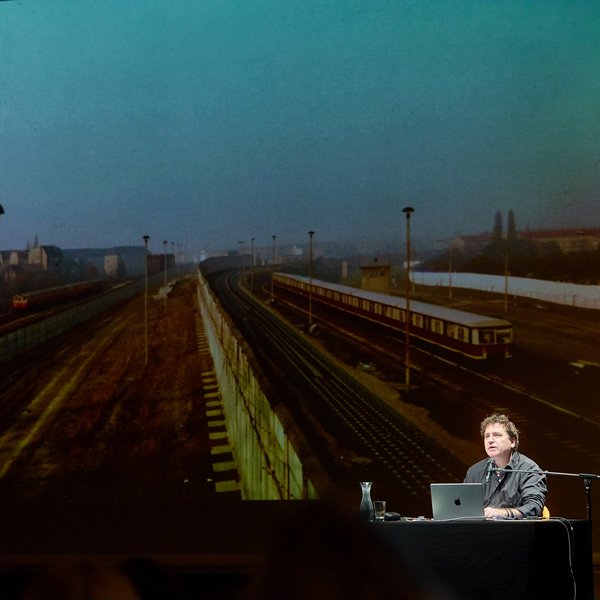 Historiker Ilko-Sascha Kowalczuk sitzt vor der Projektion von Eisenbahnschienen.