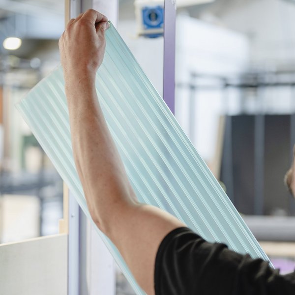 Eine Person hält eine durchsichtige Bahn der Rückwand in den Händen.