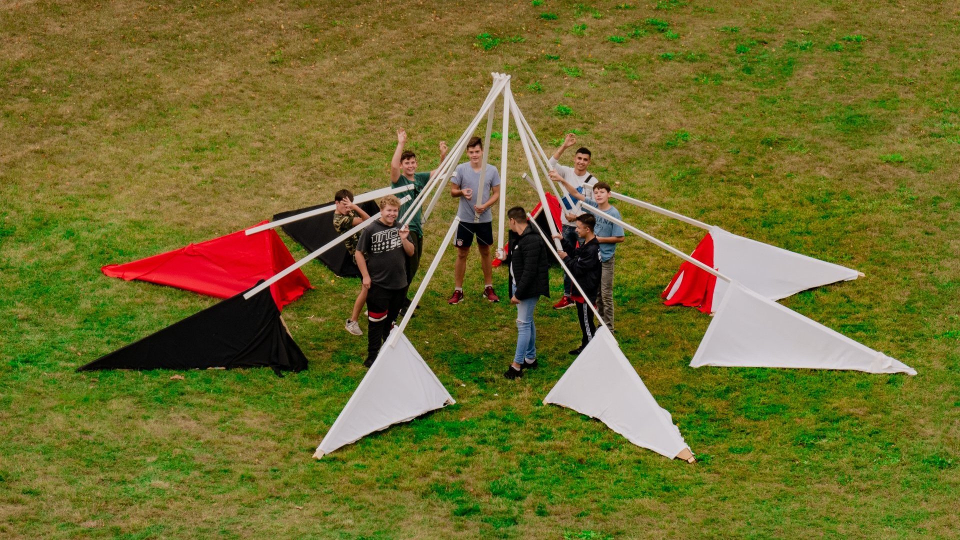 Eine Gruppe Schüler baut eine Holzkonstruktion auf einer Wiese.